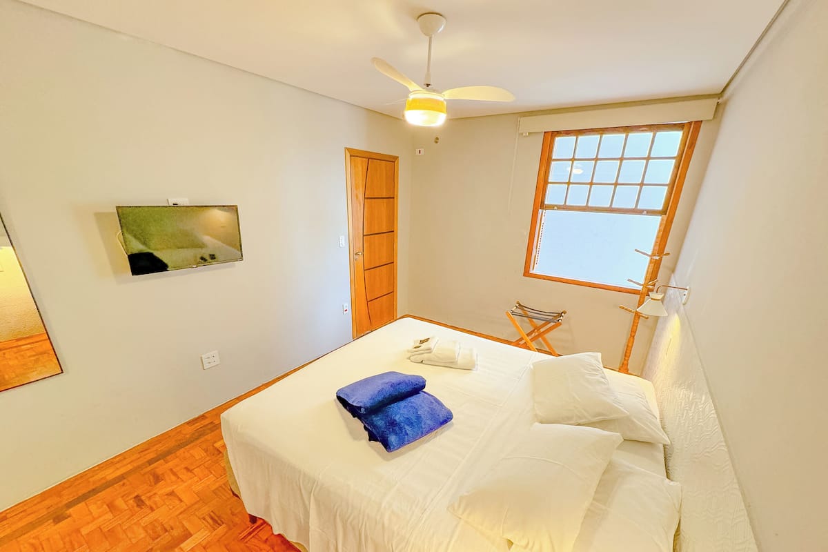 A bedroom with a bed, a ceiling fan, a window, and a wooden door.