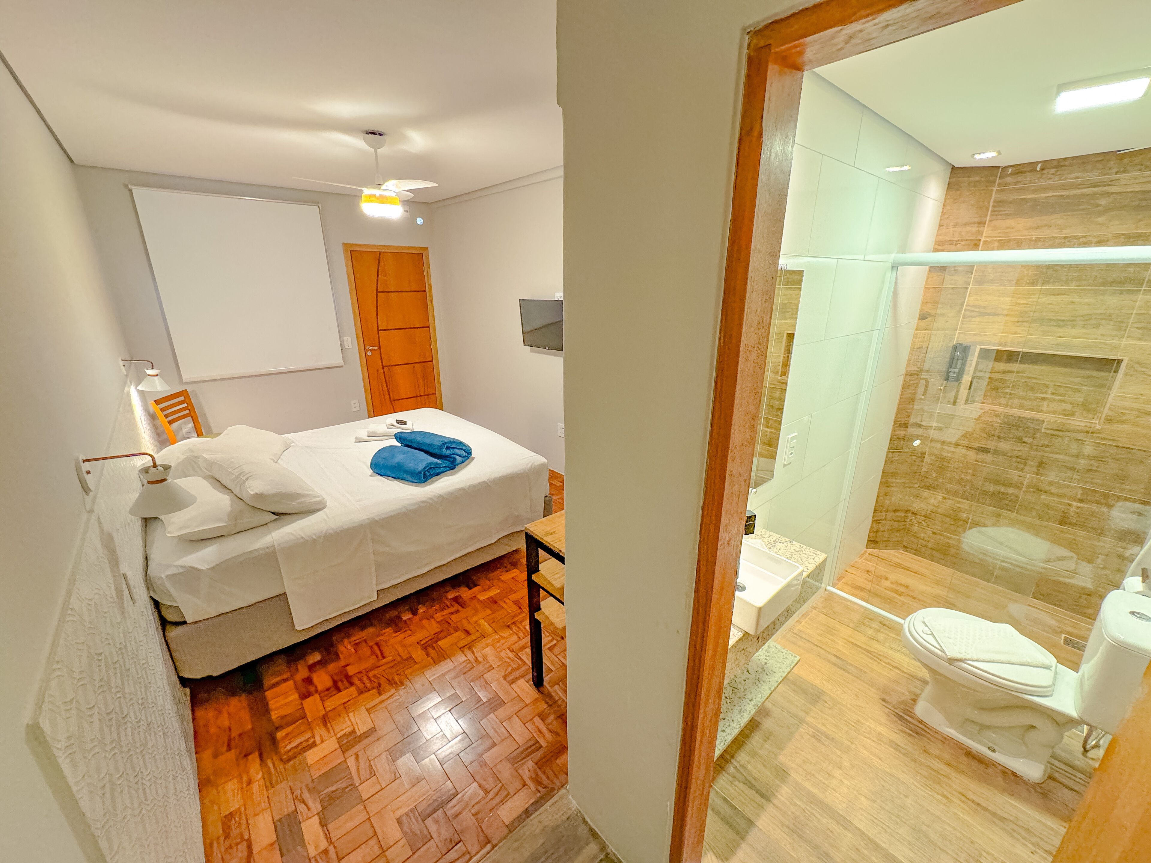 Een slaapkamer met een bed, een houten vloer, een witte muur en een houten deur.