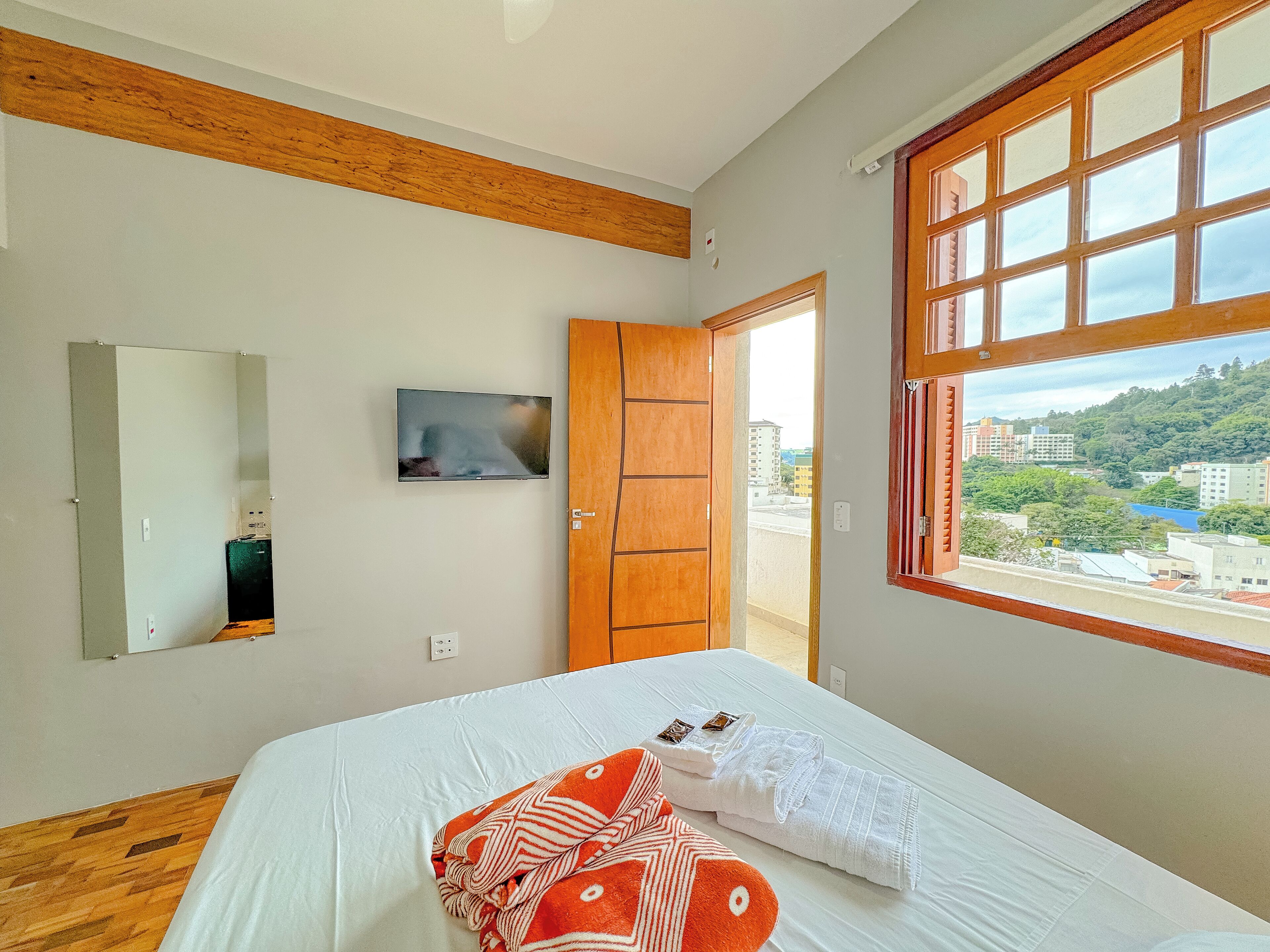 Un dormitorio con cama, televisor, techo de madera, ventana y vista a la ciudad, además de una puerta.