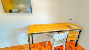 A small room with a wooden table, a white chair, a wall-mounted TV, and a water bottle on the table. - Edifício Barros (Serra Negra)
