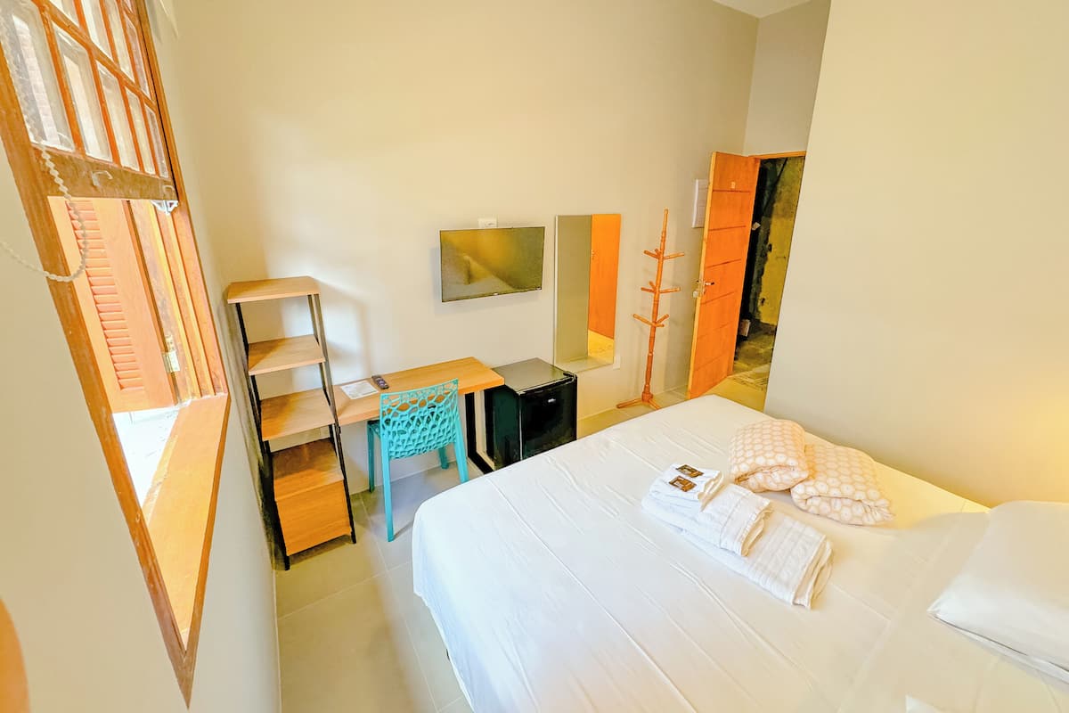 A hotel room with a bed, a desk, a chair, a TV, and a wardrobe.