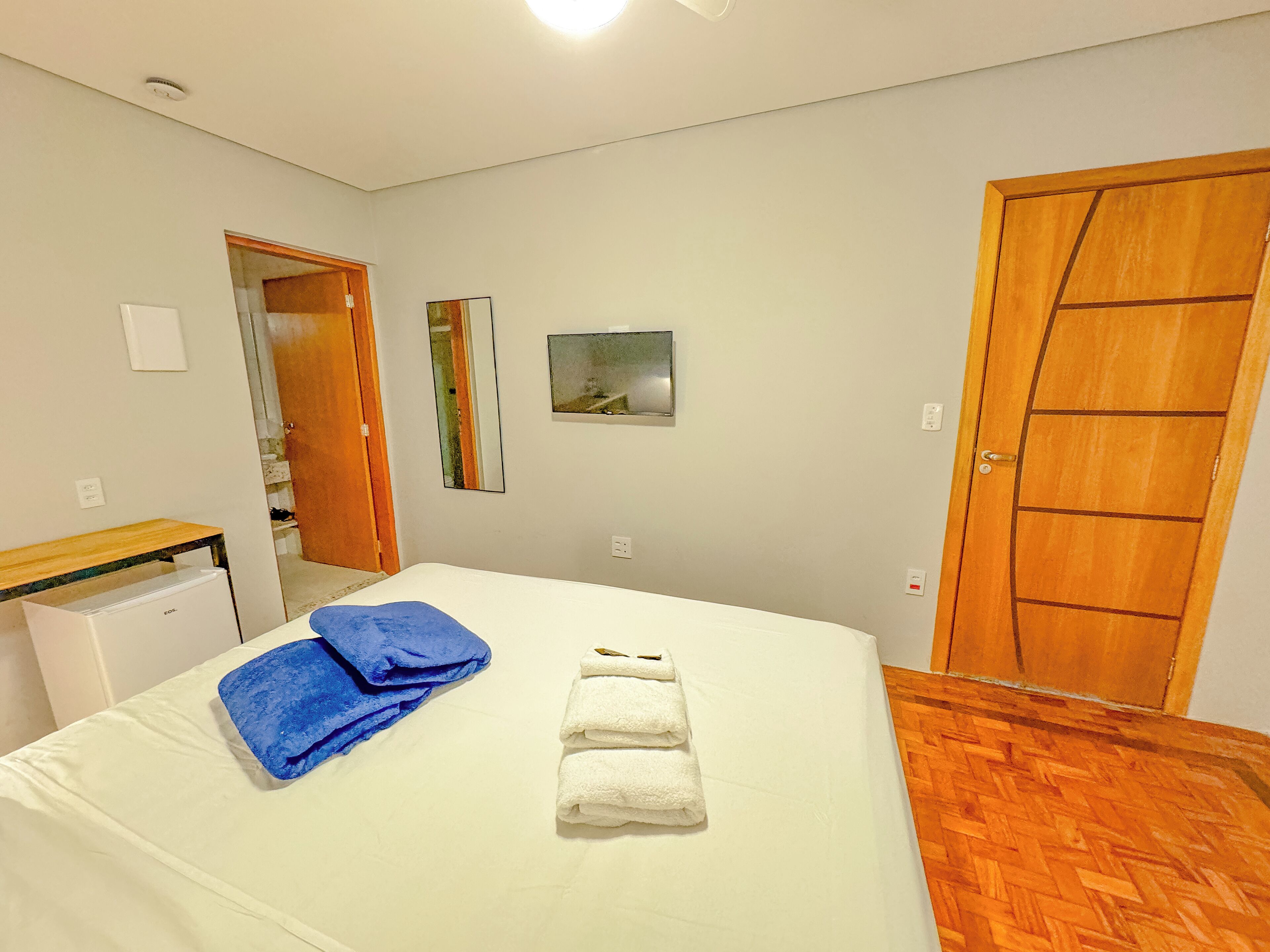 A bedroom with a bed, a wooden door, a mirror, and a small table.