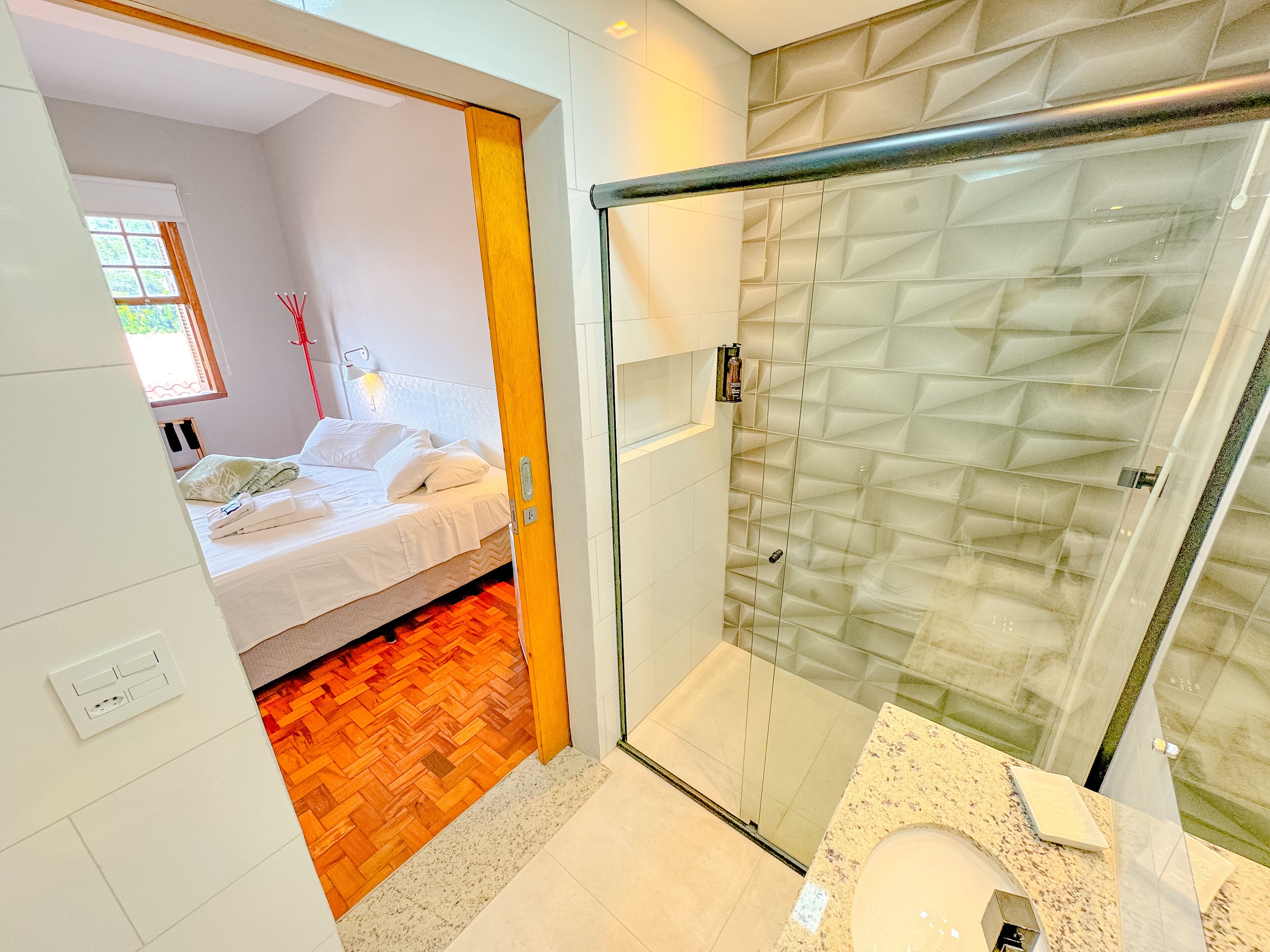 Un baño moderno con cabina de ducha de vidrio, un lavamanos blanco y suelo de madera.