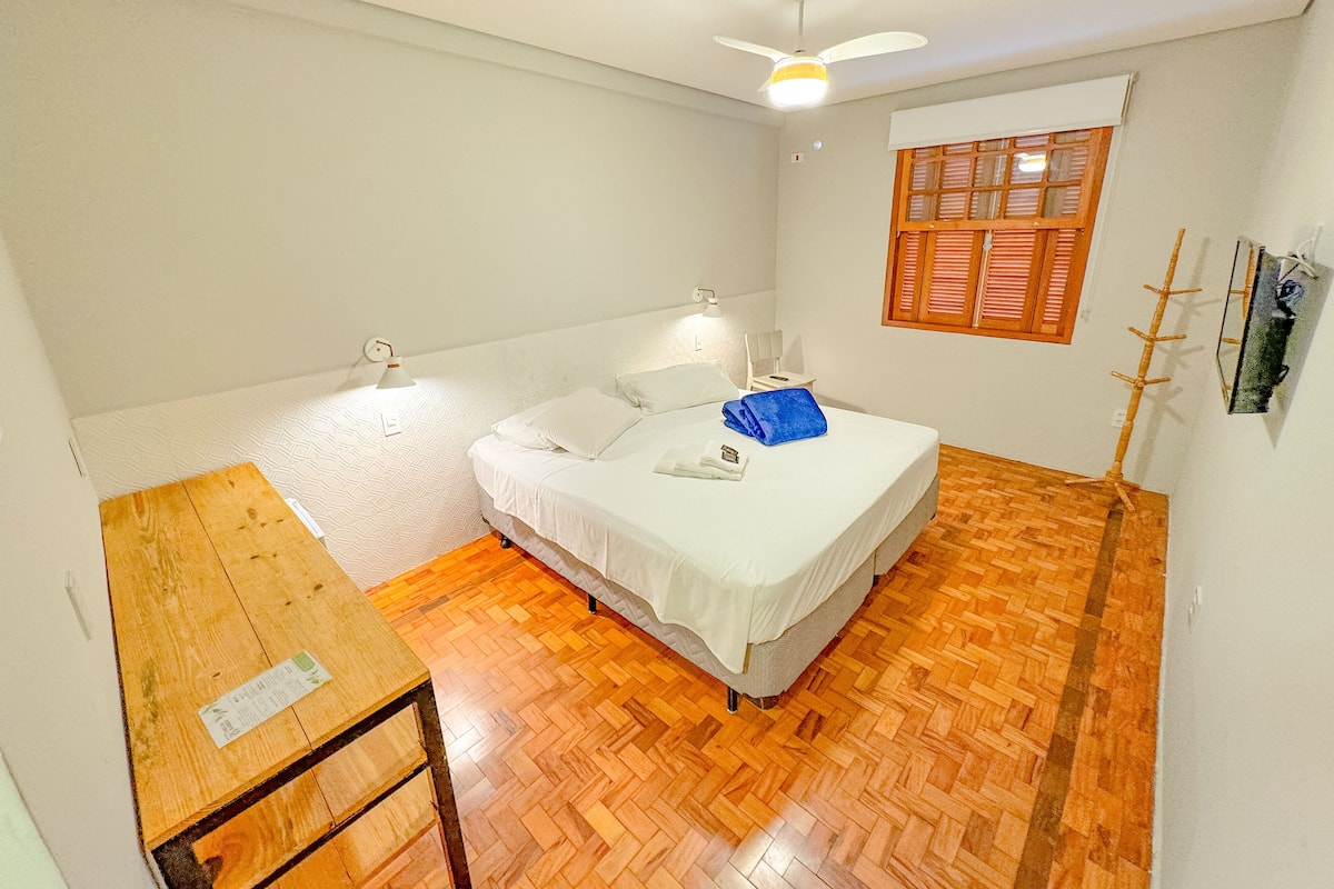 A small, clean room with a bed, a desk, and a window with shutters.
