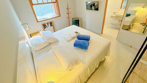 Quarto de hotel com uma cama grande, janela, espelho e televisão na parede.