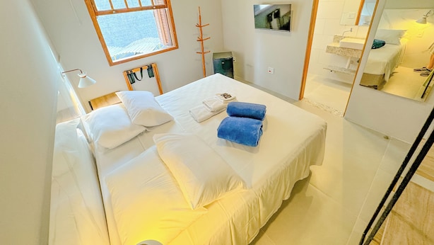 A hotel room with a large bed, a window, a mirror, and a television on the wall. - Edifício Barros (Serra Negra)