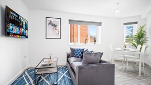 En moderne stue med en grå sofa, et glasbord og et fjernsyn monteret på væggen.