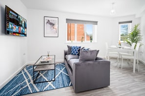 A modern living room with a grey sofa, a glass coffee table, and a TV mounted on the wall. - Luxury Two Bedroom Apartment - Parking - Smart TV (Birmingham)
