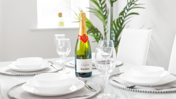 Et bord dækket til et måltid med en flaske vintage Codorniu champagne, hvide tallerkener og klare glas.