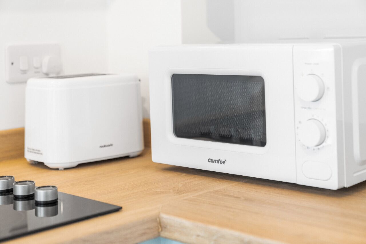 Un forno a microonde bianco Comfee con display digitale e comandi a manopola, posizionato su un piano di lavoro in legno accanto a un tostapane bianco.