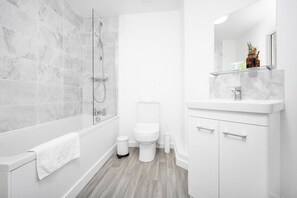 Un baño moderno con ducha envuelta en vidrio, inodoro blanco y tocador con espejo.