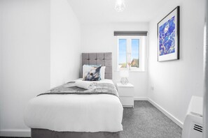Un dormitorio con una cama, una mesita de noche, una lámpara, una obra de arte enmarcada y una ventana con vistas.
