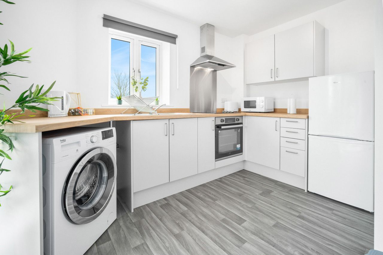 Una cucina moderna con mobili bianchi, una cappa in acciaio inossidabile, forno a incasso, microonde e lavatrice.