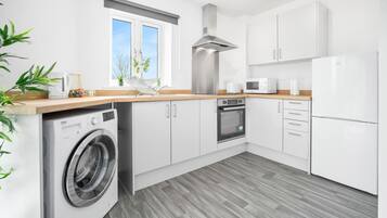 Una cucina moderna con mobili bianchi, una cappa in acciaio inossidabile, forno a incasso, microonde e lavatrice.