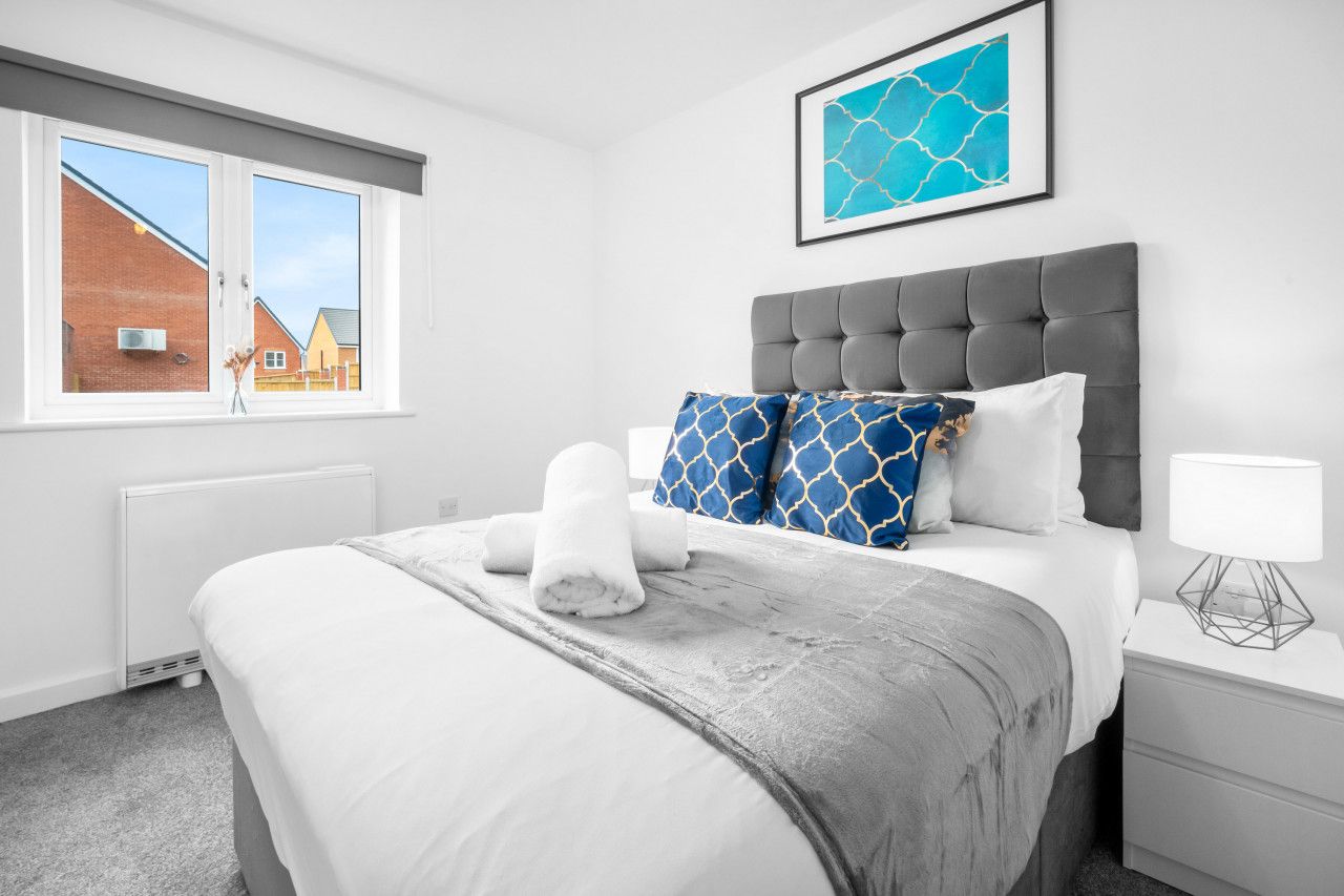 Quarto de hotel com cabeceira estofada cinza, roupa de cama branca, uma obra de arte emoldurada sobre a cama e vista para um edifício de tijolos pela janela.
