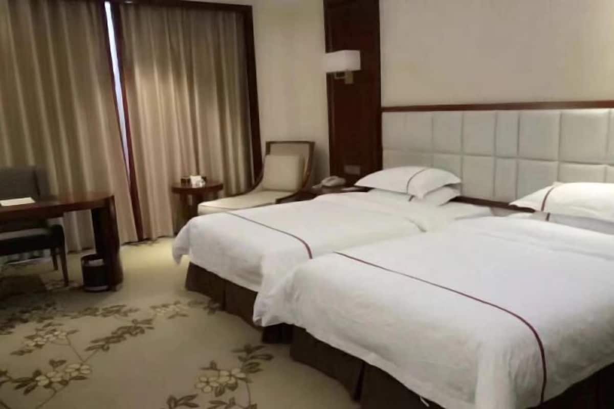 Habitación de hotel con dos camas, un escritorio, una silla, una mesita de noche y un ventanal con cortinas.