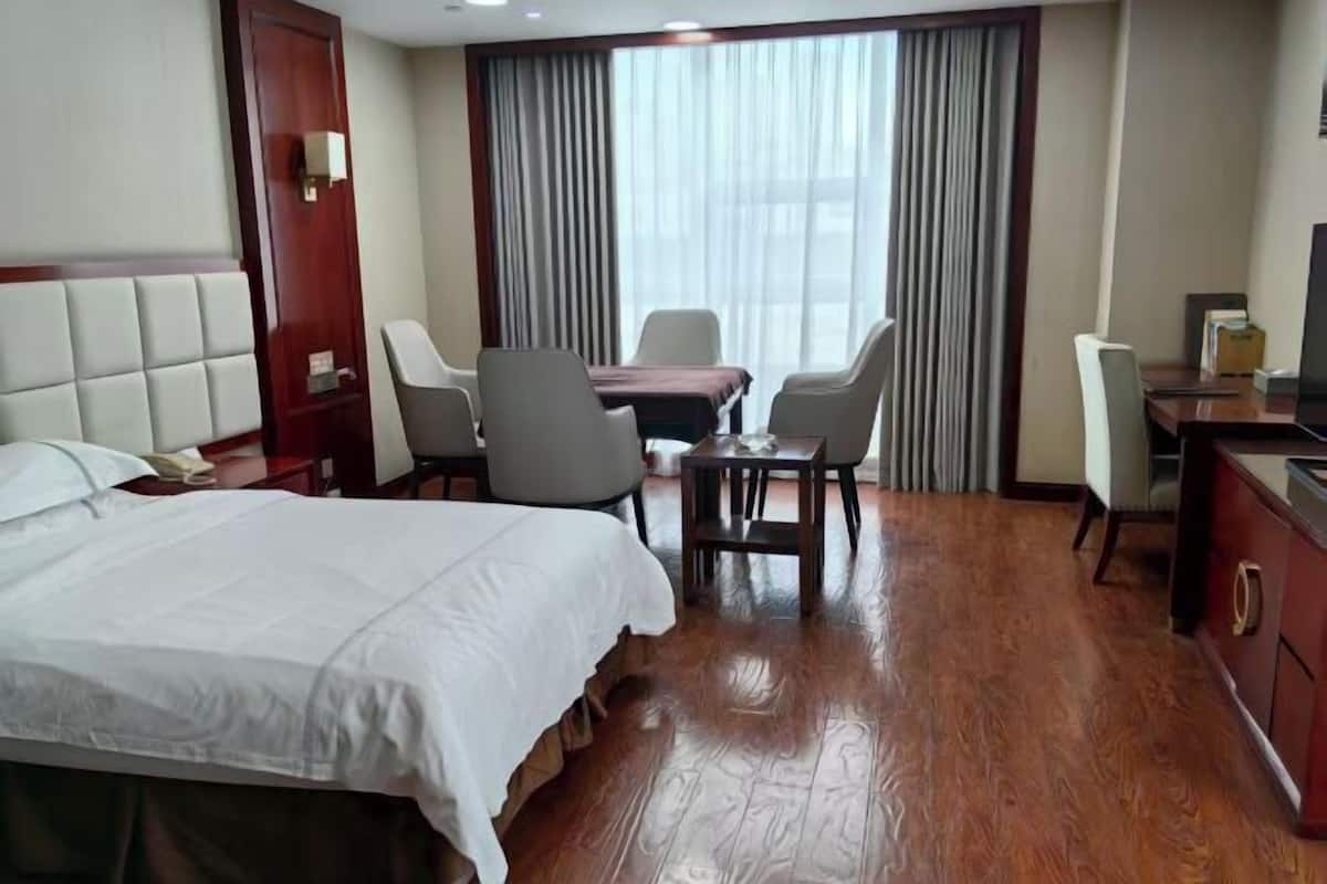 Habitación de hotel con cama, escritorio, dos sillas, mesa, televisión y ventana con cortinas.
