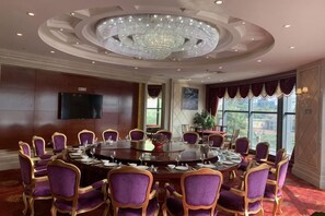 Un salón de conferencias con una mesa redonda, sillas moradas, una araña y un televisor en la pared.