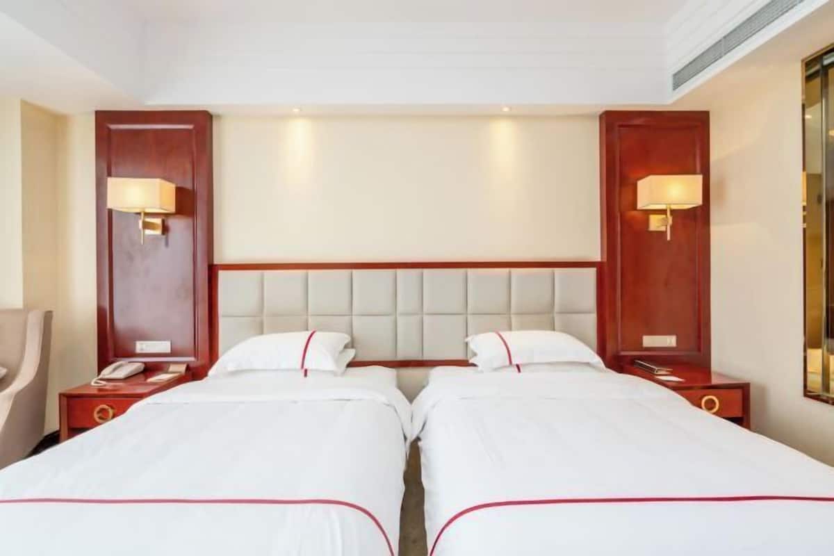 Una habitación de hotel con dos camas, cabeceros de madera, lámparas de noche, una mesita de noche con teléfono y un espejo.