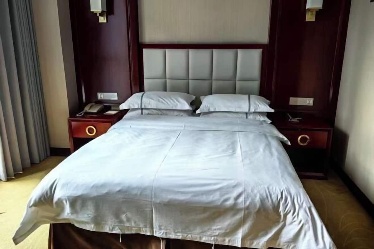 Una habitación de hotel con una cama grande, dos mesitas de noche, un teléfono y una mesilla.