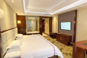 Ein Hotelzimmer mit einem großen Bett, einem Fernseher, einem Schreibtisch und einem Spiegel.