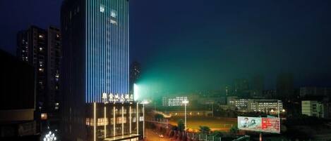 Un edificio de gran altura con señalización iluminada, rodeado de un entorno urbano bien iluminado.