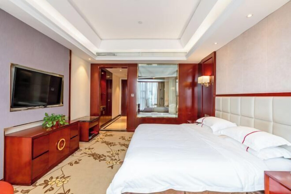 Ein Hotelzimmer mit einem großen Bett, einem Fernseher, einem Spiegel und einer hölzernen Kommode.