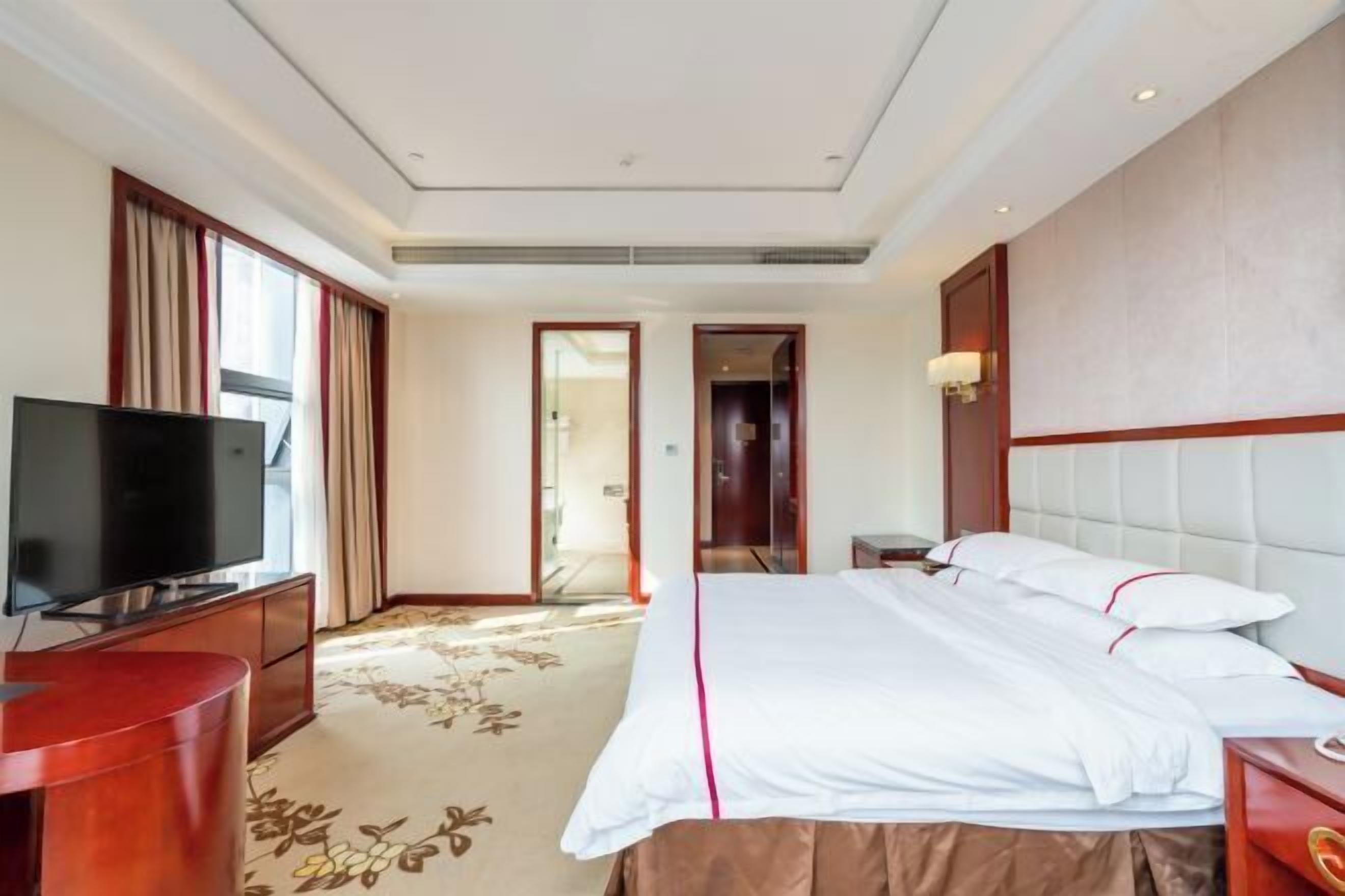 A hotel room with a bed, a television, a desk, and a carpeted floor.