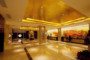 Een hotel lobby met een receptiebalie, een grote decoratieve wand en een gepolijste vloer.