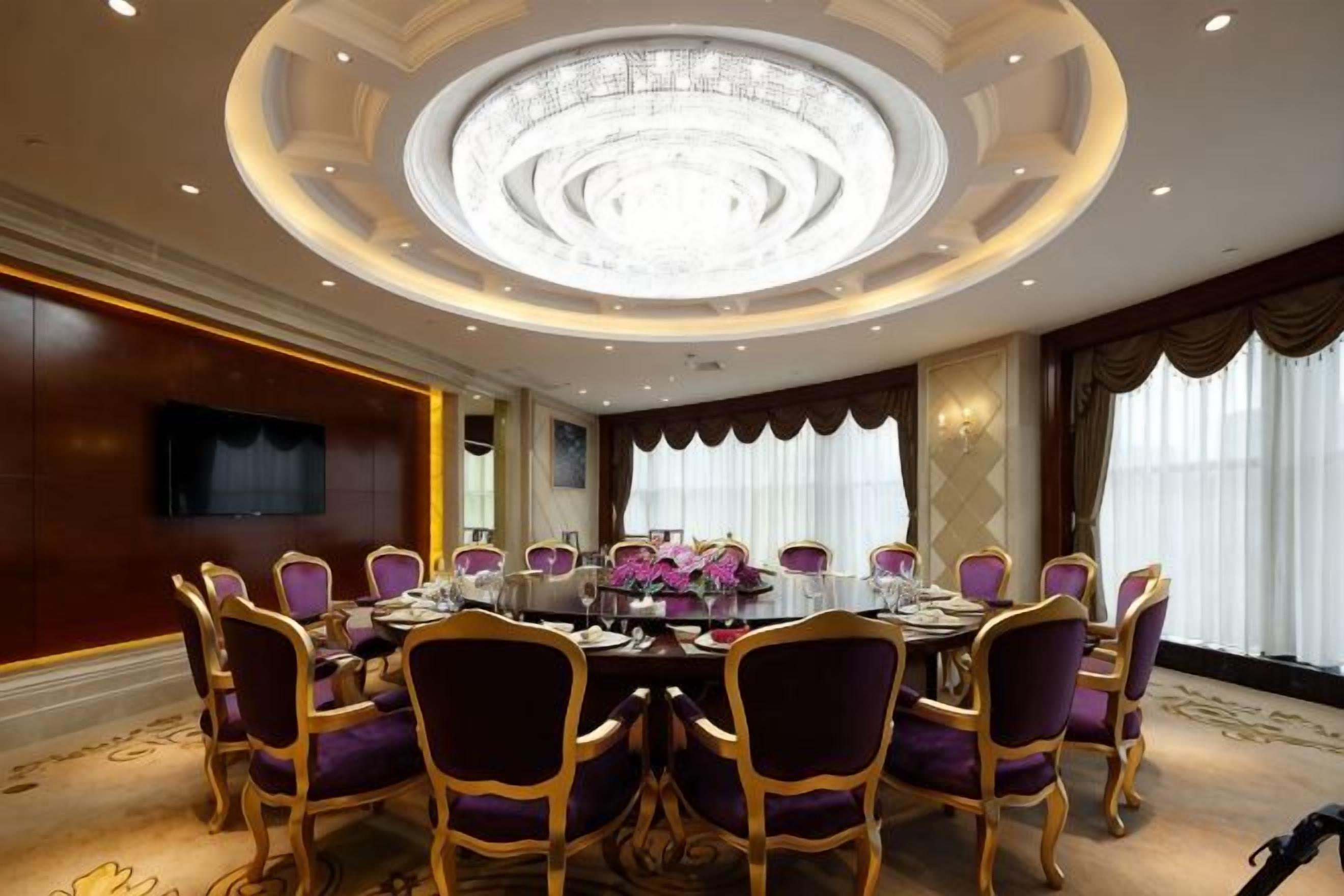 A conference room with a round table, purple chairs, and a chandelier.