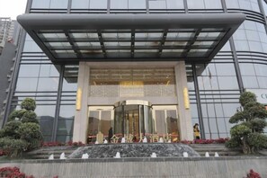 Un bâtiment moderne doté d’une façade en verre, d’un hall d’entrée abrité et d’un élément décoratif aquatique à l’avant.