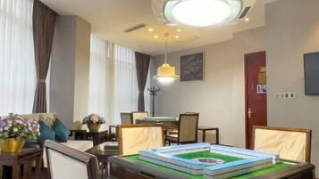 Quarto de hotel com área de jantar, uma mesa com toalha verde e luminária suspensa.