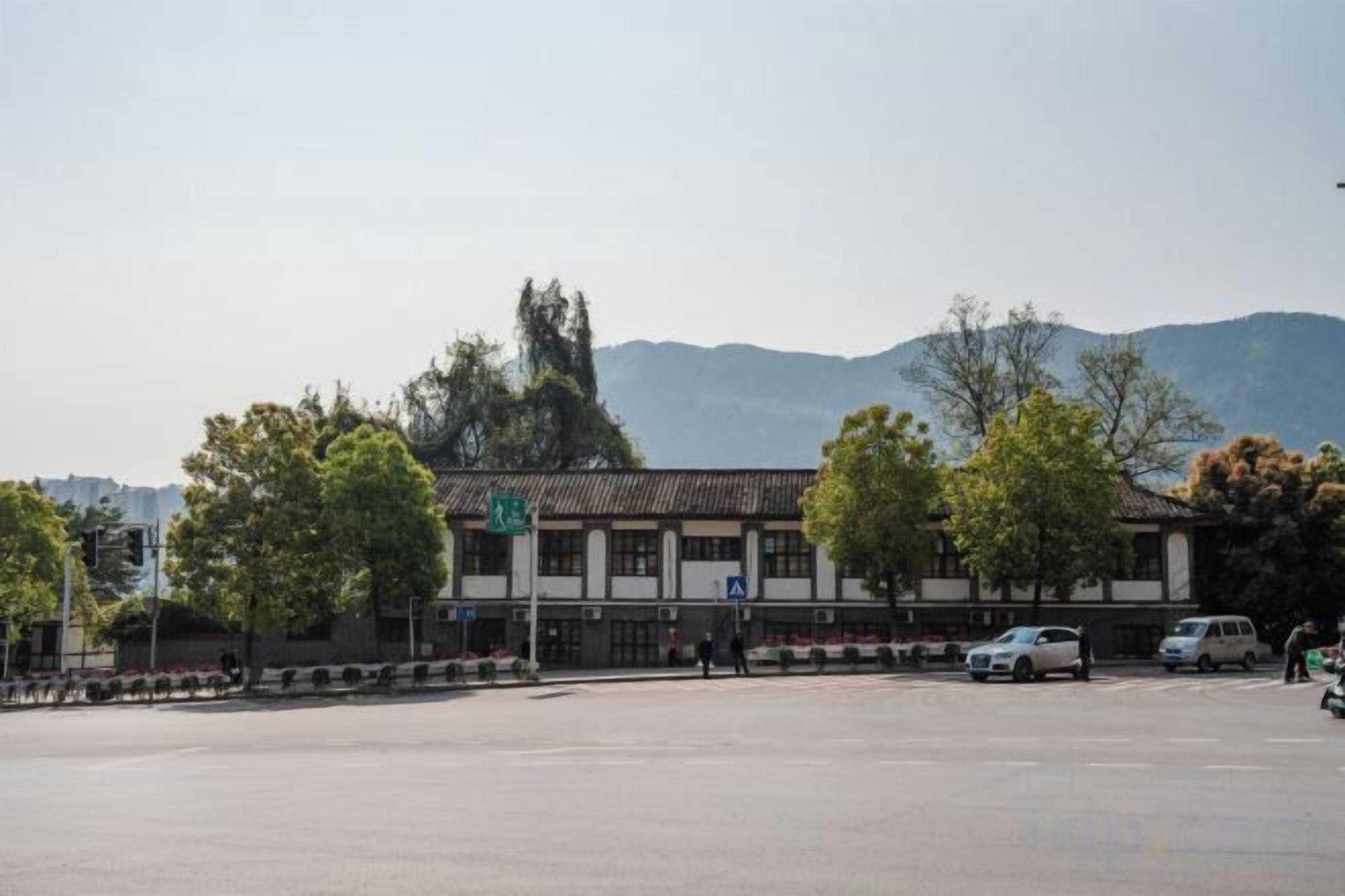 A parking lot with a building in the background, trees, and mountains in the distance.