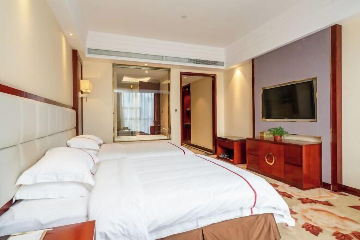 Ein Hotelzimmer mit einem großen Bett, einem an der Wand montierten Fernseher, einem Spiegel und einer Kommode.