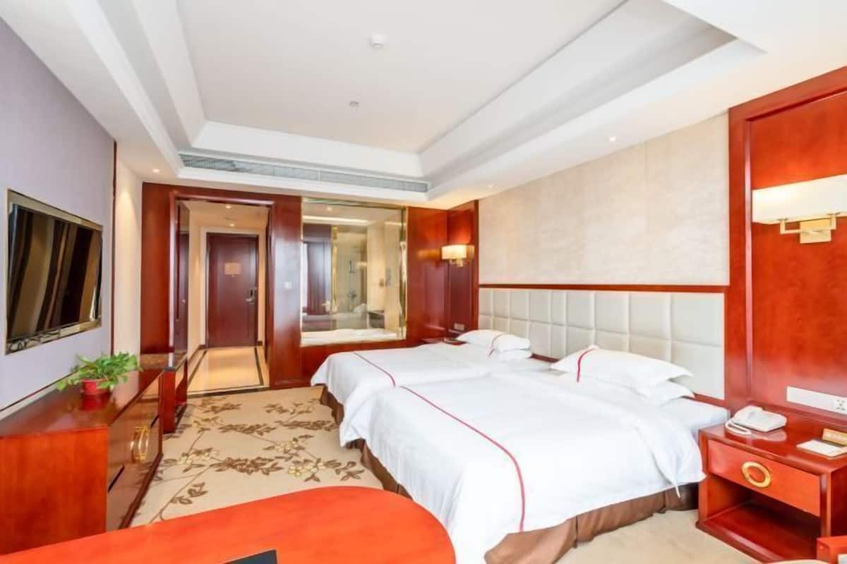 Una habitación de hotel con dos camas, una mesita de noche de madera, un escritorio con lámpara y un espejo grande.
