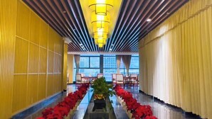 Un pasillo de hotel con paredes amarillas, una planta en el centro y una fila de flores rojas.