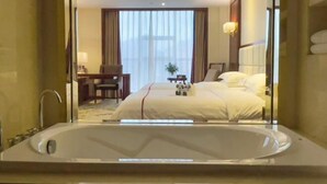 Habitación de hotel con una bañera grande, una cama con ropa blanca, un escritorio con una silla y una ventana con cortinas.
