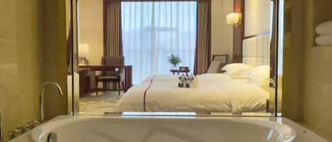 A hotel room with a large bathtub, a bed with white linens, a desk with a chair, and a window with curtains.