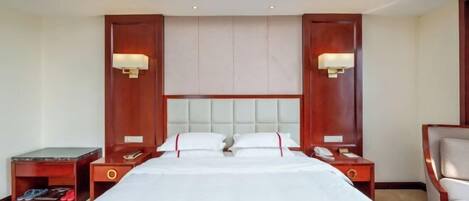 A hotel room with a large bed, two bedside tables, a nightstand, and a chair.