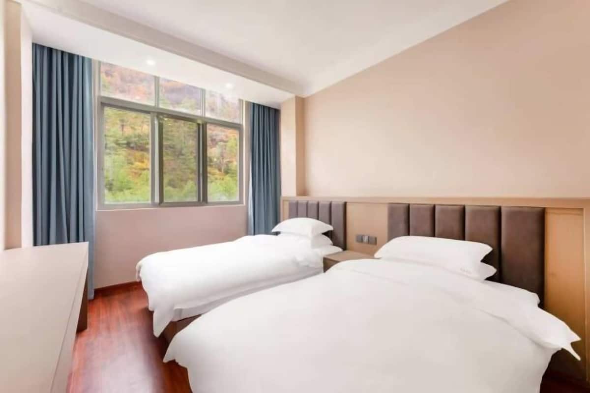 Une chambre d’hôtel avec deux lits, une grande fenêtre et un plancher en bois.