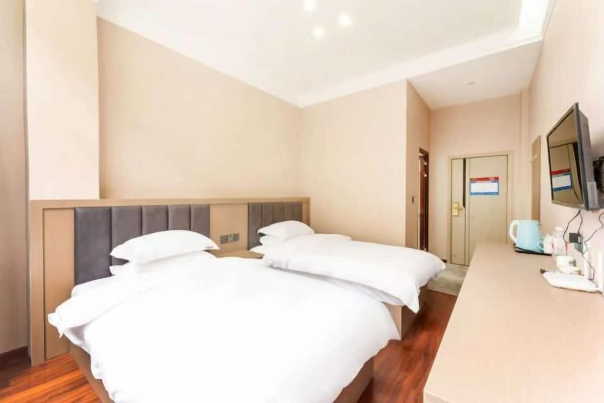 Une chambre d’hôtel avec deux lits, un bureau en bois, une télévision et une porte avec une pancarte.