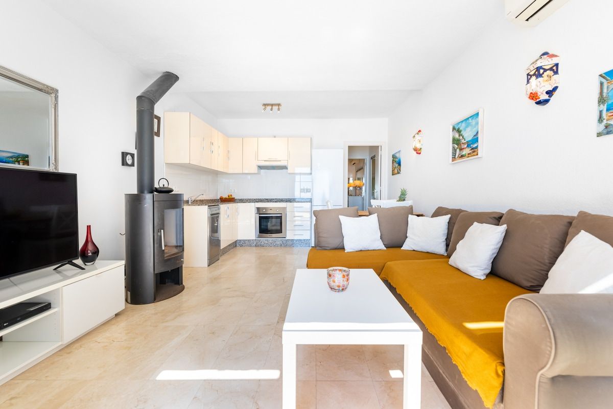 A modern living room with a flat-screen TV, a white coffee table, and a sofa with a mustard throw.