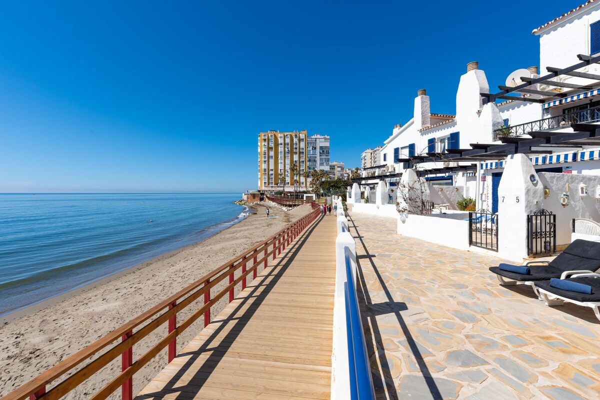 A coastal promenade with a wooden walkway, beach, and seaside buildings.