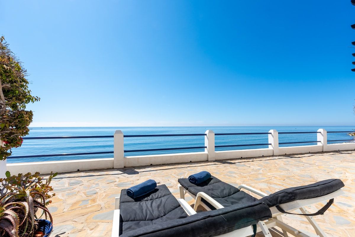 Een terras met lounge fauteuils en uitzicht op zee.