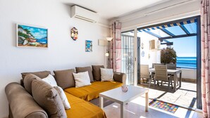 Een moderne woonkamer met een bank, een bijzettafeltje en uitzicht op zee door een open deur.