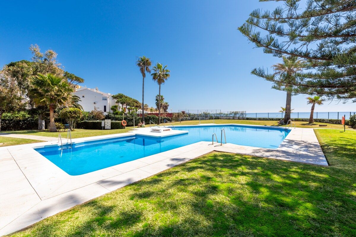 A swimming pool with a clear blue water, surrounded by grass and trees, with a building in the background.