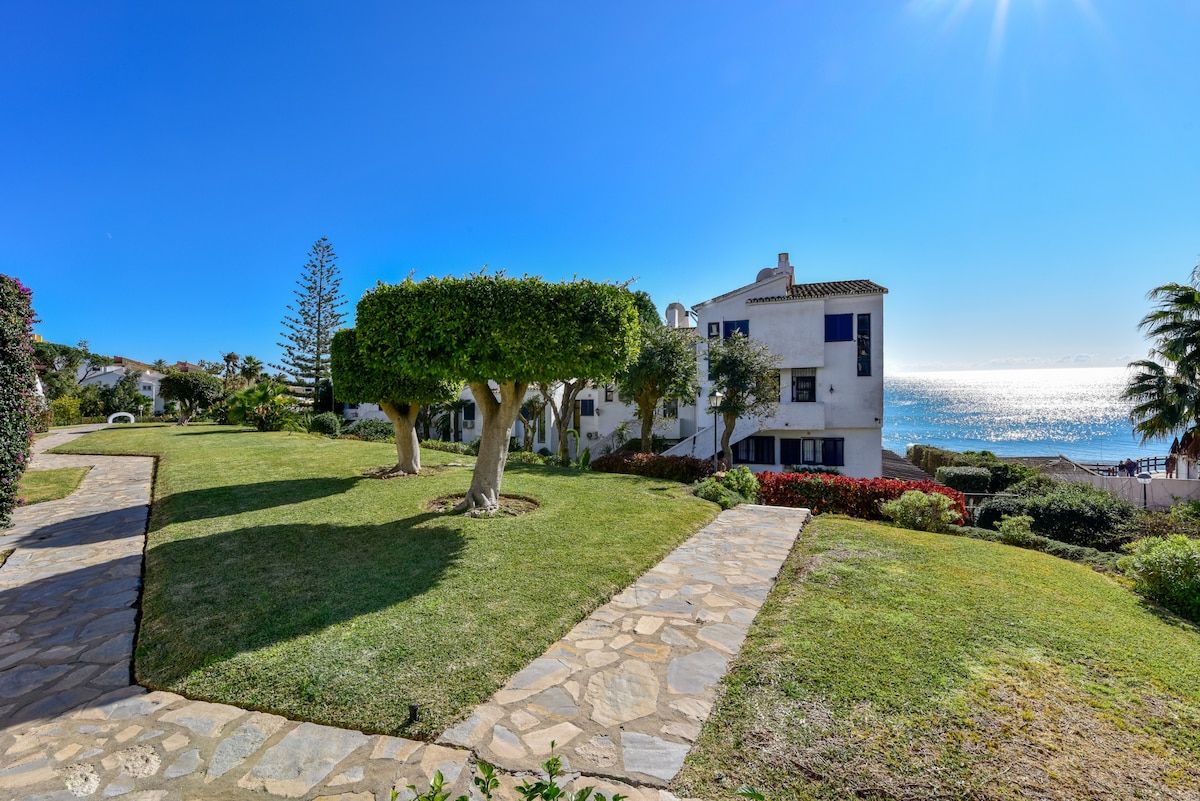 A coastal property with a stone pathway, manicured lawn, and a building with a white facade.