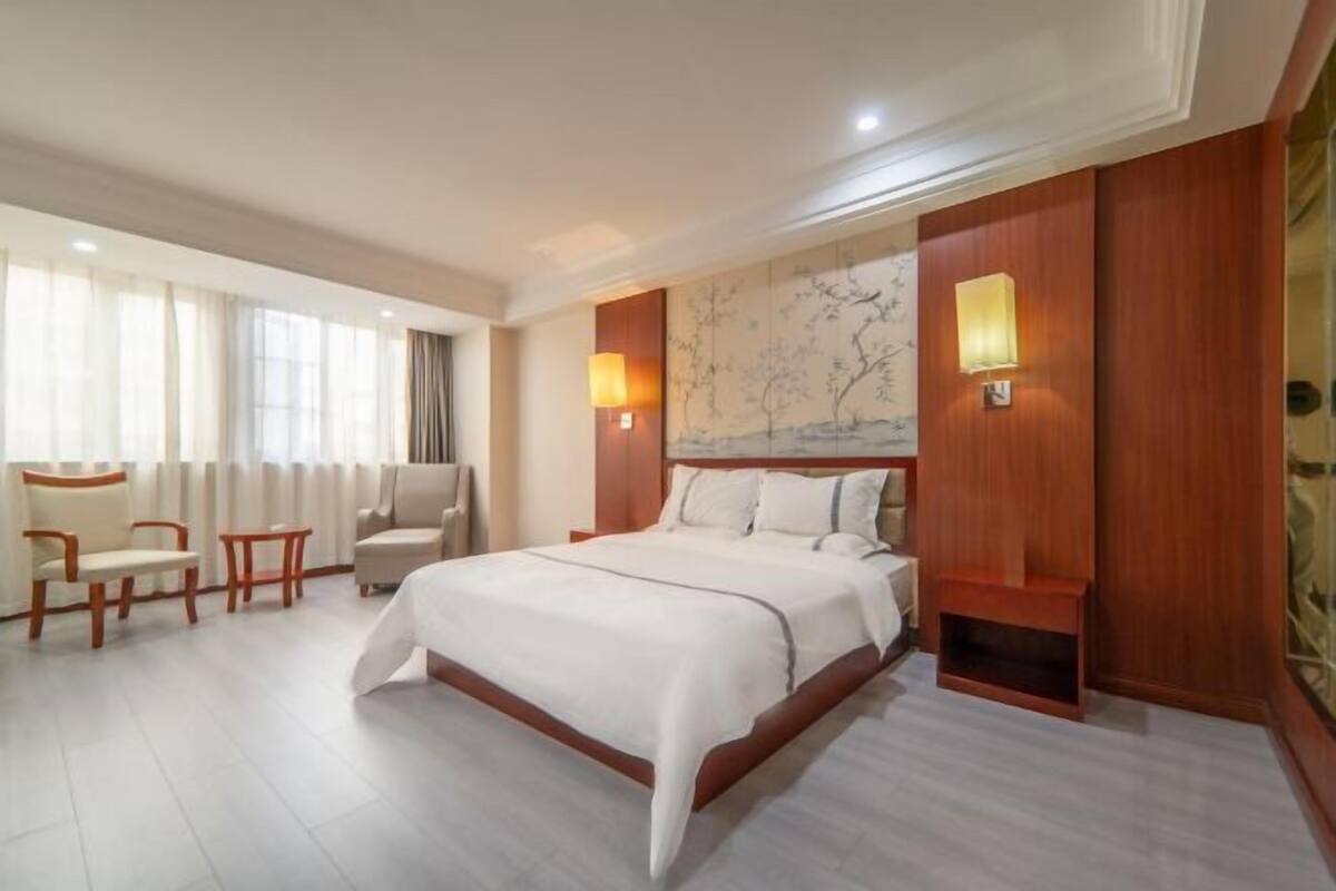 A hotel room with a large bed, two bedside tables, a chair, and a small table.