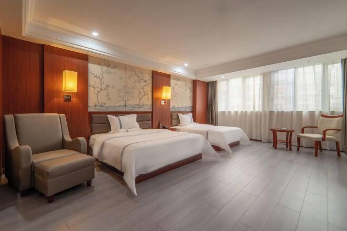 A hotel room with two beds, a sofa, a chair, and a large window with curtains.