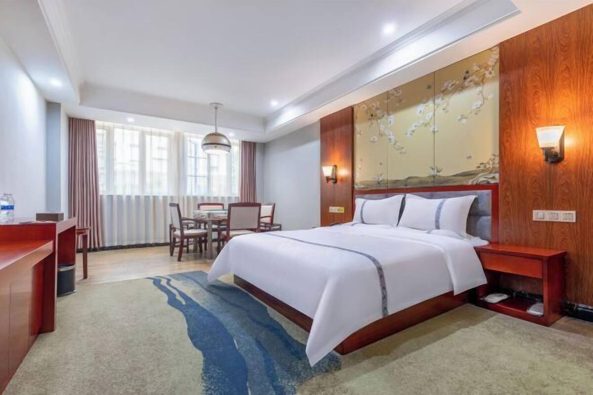 A hotel room with a bed, desk, chair, and a wall with a floral design.